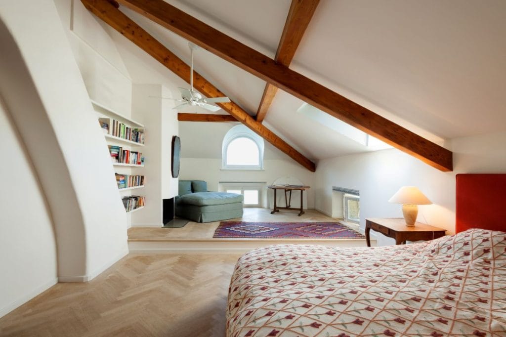 L-shaped loft conversion guest room with wood finishes, inbuilt bookshelf, and light flooring